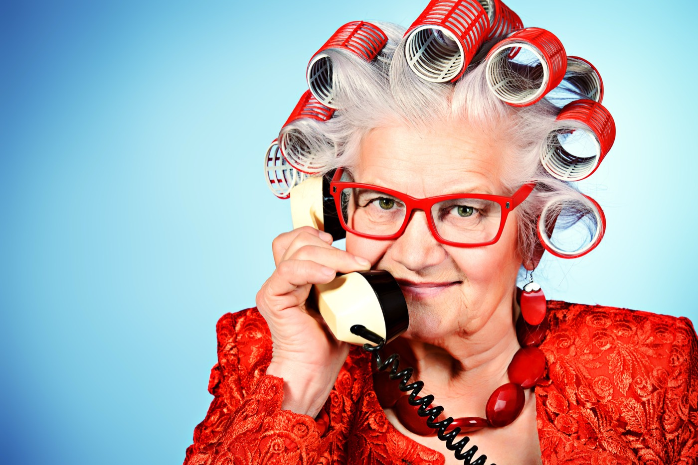 Smiling woman in red glasses and hair curlers chatting on the phone
